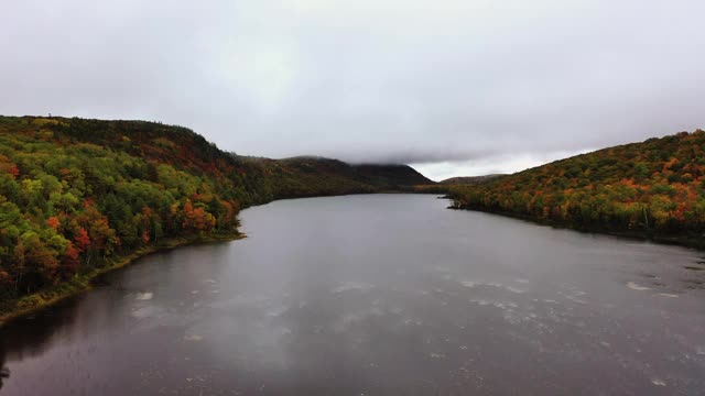 美丽的旅行，空中的云湖和树木覆盖的海岸线在一个多云的早晨与色彩缤纷的秋天树叶和常青树覆盖的山。视频素材