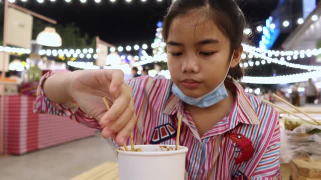 4K，亚洲女孩吃泰国街头食物叫Isan火锅与猪肉在夜市在人们走视频素材