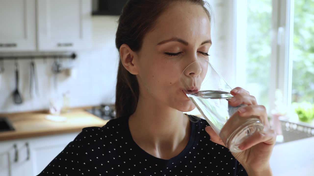 年轻的20多岁的欧洲女孩喝纯净的静态水在厨房。视频素材