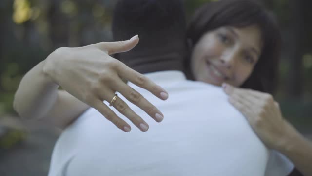 特写:白人女性手拿订婚戒指，模糊女子拥抱非裔美国人在背景。快乐的女人在户外炫耀珠宝。异族通婚的概念。视频素材