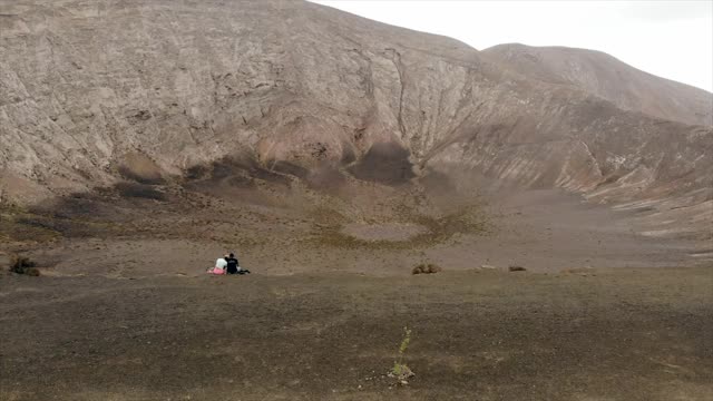 一对夫妇坐在美丽的西班牙兰萨罗特岛布兰卡火山边缘的航拍镜头视频素材