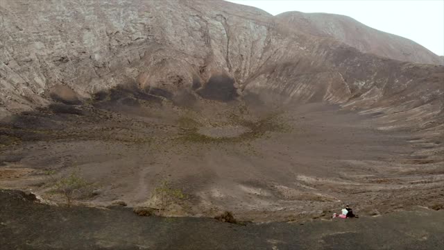 鸟瞰图/无人机镜头一对夫妇坐在美丽的西班牙兰萨罗特岛的火山边缘视频素材