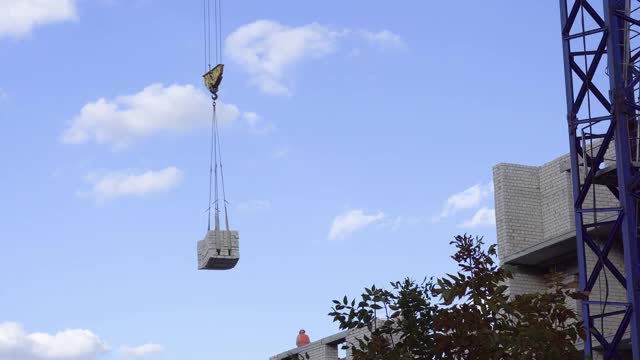 建筑起重机将货物运送到建筑工地。一座未完工的白砖建筑。视频素材