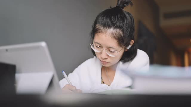 亚洲学校十几岁的女孩早上醒来看书，用笔记本电脑听音乐，学习，教育，在家自学视频素材