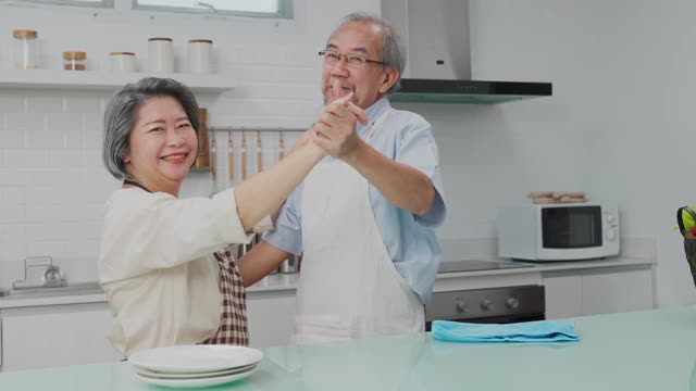 夫妇老亚洲长者幸福生活在家庭厨房。爷爷奶奶跳着幸福的舞蹈，微笑着享受退休生活。老年人的家庭关系和活动概念。视频素材