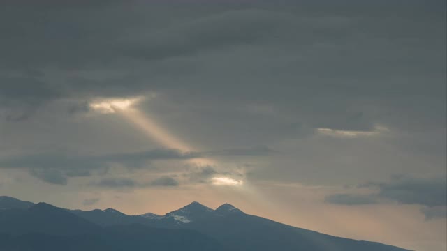 风暴云移动与太阳光束在黑暗的天空越过山脉的视频时间流逝视频素材