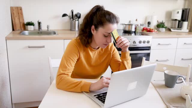 女人在网上购物，用金卡付款。年轻女孩坐在笔记本电脑上上网购买输入信用卡细节厨房室内背景。网上购物电子商务概念视频素材