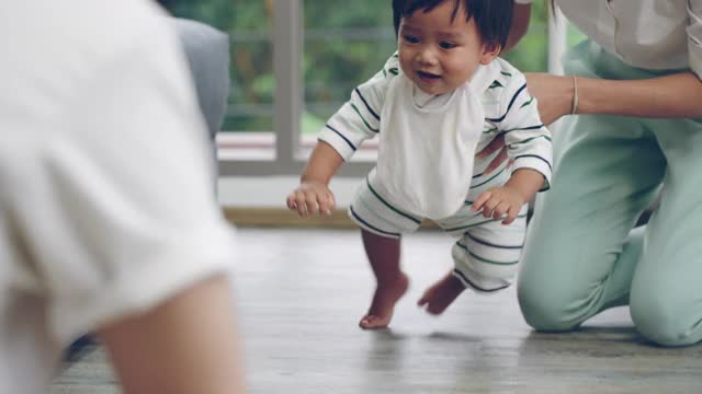 亚洲婴儿的第一步。母亲牵着孩子的手走在家里的客厅里。家庭支持小孩。宝宝在学走路视频素材