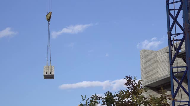 建筑起重机将货物运送到建筑工地。一座未完工的白砖建筑。视频素材