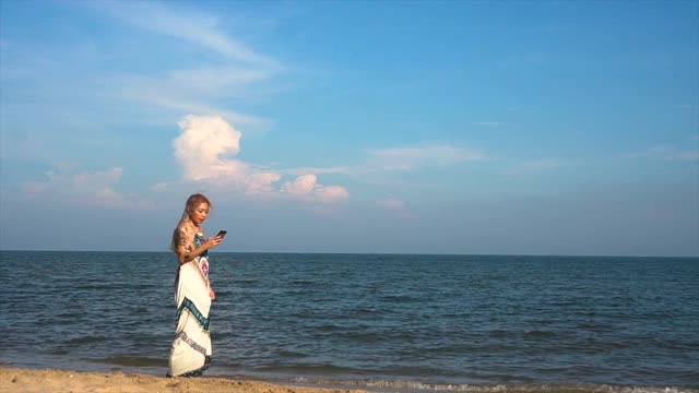 一名女子在海滩上用智能手机散步并拍照。视频素材