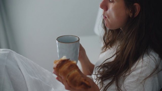 清晨，一位黑发女子正吃着羊角面包和咖啡。一个女人的特写视频素材