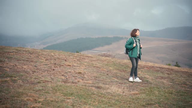 一个背着背包的年轻女子走在山顶上，可以看到山谷视频素材