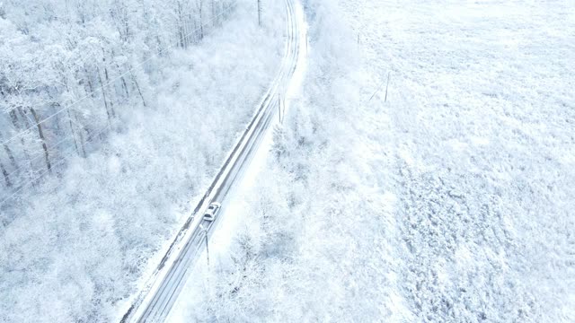 汽车在白雪覆盖的森林周围行驶的鸟瞰图视频素材