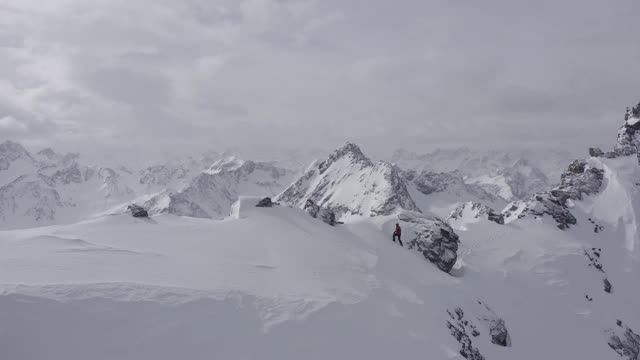 在奥地利阿尔卑斯山脉，一名登山者正走在冰雪覆盖的山脊上，雪花吹在他的脸上视频下载