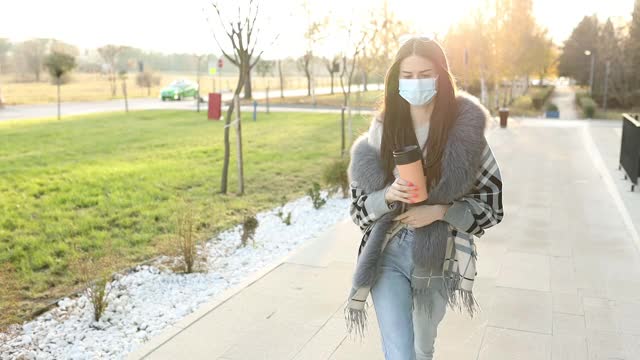 美丽优雅的女学生戴着防护面具，拿着咖啡杯和手机在校园里视频素材