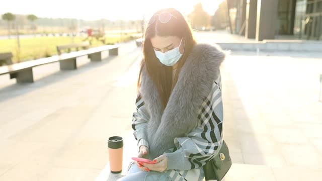 美丽优雅的女学生戴着防护面具，拿着咖啡杯和手机在校园里视频素材