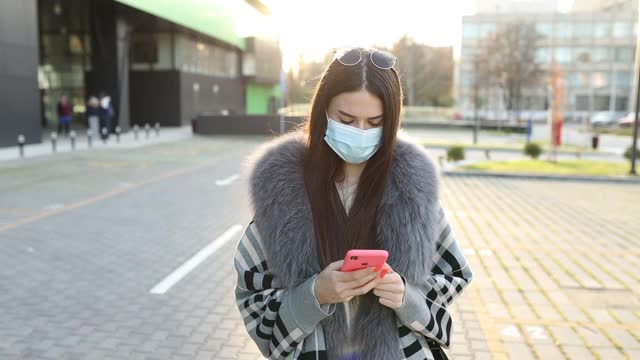 美丽优雅的女学生戴着防护面具，拿着咖啡杯和手机在校园里视频素材