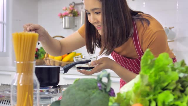 年轻的亚洲妇女在厨房做饭。视频素材