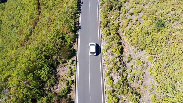 4K无人机拍摄的小白色掀背车在两座森林中间的空旷道路上行驶的画面视频素材