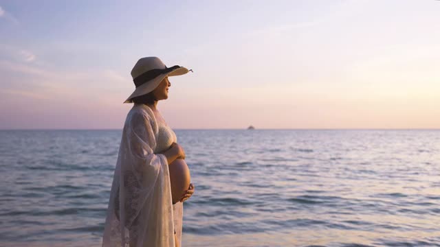 年轻的亚洲孕妇放松散步在海滩上日落视频素材