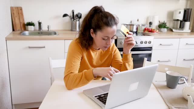 女人在网上购物，用金卡付款。年轻女孩坐在笔记本电脑上上网购买输入信用卡细节厨房室内背景。网上购物电子商务概念视频素材