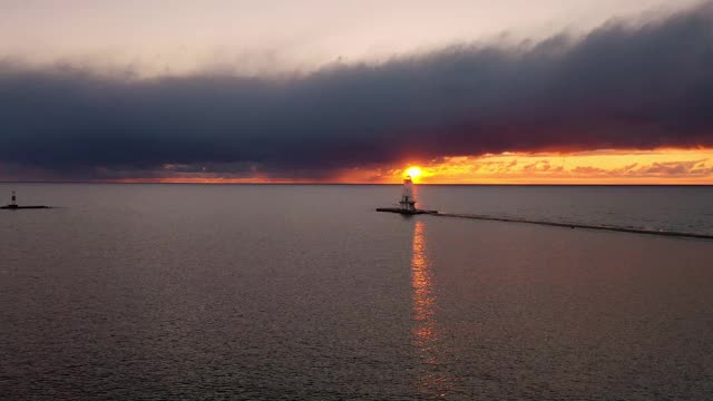 夕阳空中飞向卢丁顿防波堤灯塔，明亮的黄色太阳从云下创造一个美丽的橙色天空和反射在水面上。视频素材