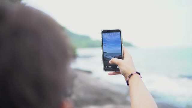 亚洲女人在海滩的岩石上拍摄海景。视频素材