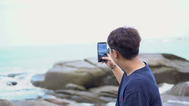 亚洲女人在海滩的岩石上拍摄海景。视频素材