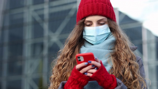 特写美丽的白种人年轻的卷发女性在医疗面具手机短信。一个白人女人在用智能手机浏览，然后看向别处。在线，社交网络视频素材