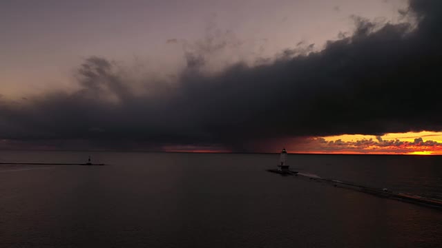 美丽的日落空中的白色卢丁顿防波堤灯塔与灯光闪烁，粉红色和橙色的天空和云反射在密歇根湖的水。视频素材