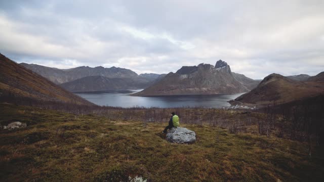 坐在岩石上看峡湾和山脉的徒步旅行者视频素材