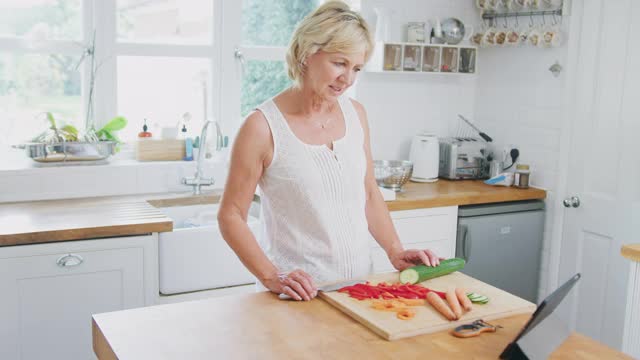 退休的高级妇女在厨房里按照数字片切食材的食谱做饭视频素材