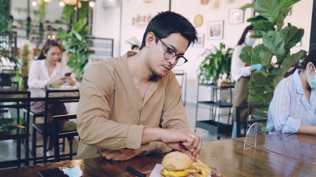 年轻的亚洲男子分开坐在餐厅吃食物和保持社交距离视频素材