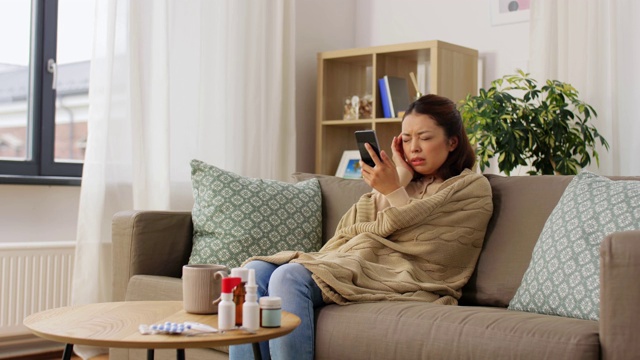 可怜的生病女人裹着毯子在家用智能手机视频素材