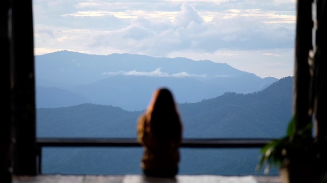 慢动作模糊的后视图，一个女性旅行者坐在看一个美丽的山和自然景观日落前视频素材