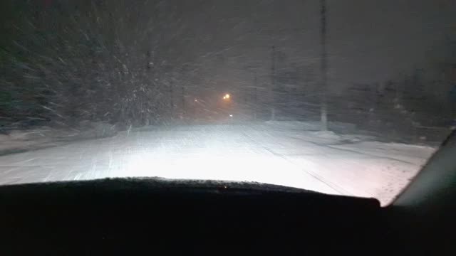 一辆在暴风雪中行驶的汽车的前挡风玻璃的内部视图。空的夜晚。潮湿的雪落在前面的玻璃和挡风玻璃的雨刷上清洁它。视频素材