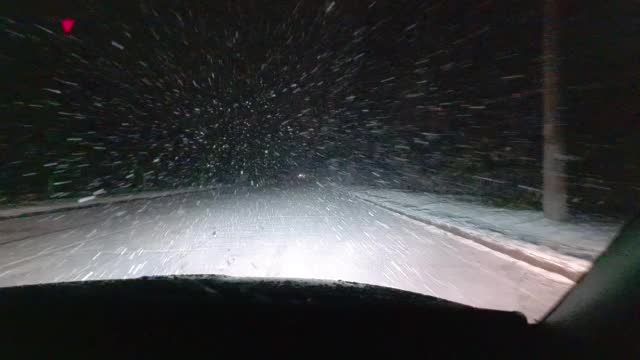 一辆在暴风雪中行驶的汽车的前挡风玻璃的内部视图。空的夜晚。潮湿的雪落在前面的玻璃和挡风玻璃的雨刷上清洁它。视频素材