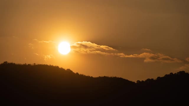 夕阳从傍晚的山天际线而阳光反射云已经改变了他们的形状，因为被风吹。从而产生温暖的橙色光芒视频素材