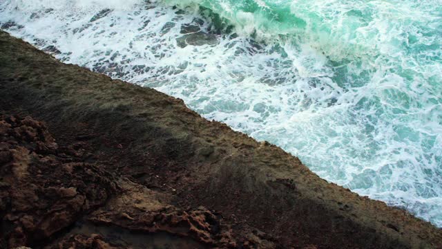 海浪在绿色的海水撞击岩石海岸的慢动作视频，从上面观看视频素材