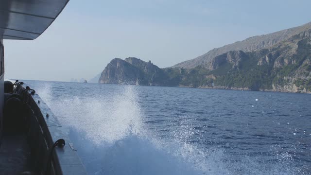 摩托艇沿着多山的海岸行驶。从甲板上看，白色飞溅视频素材