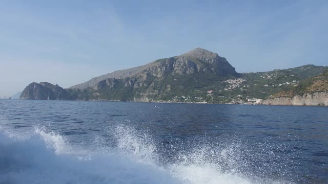 船沿着多岩石的海岸快速地漂着。山坡上的小村庄。阿玛海岸,意大利视频素材