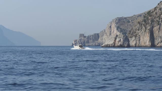 一艘小型摩托艇漂浮在意大利海岸线的岩石上。蓝色海面上的悬崖视频素材