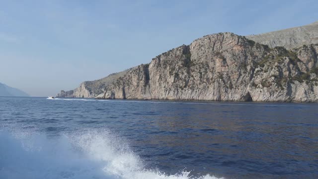 摩托艇漂浮在布满岩洞的岩石峭壁上，留下白色的泡沫痕迹。蓬康巴内拉,意大利视频素材