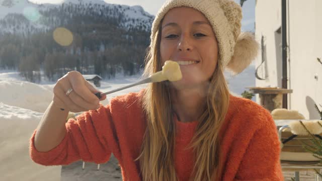 快乐的年轻女子吃芝士火锅在瑞士享受阿尔卑斯山和雪山在冬季假期。人们的饮食传统地方观念视频素材