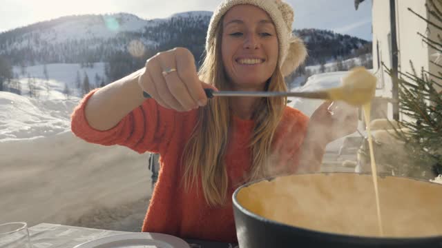 快乐的年轻女子吃芝士火锅在瑞士享受阿尔卑斯山和雪山在冬季假期。人们的饮食传统地方观念视频素材