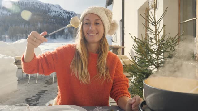 快乐的年轻女子吃芝士火锅在瑞士享受阿尔卑斯山和雪山在冬季假期。人们的饮食传统地方观念视频素材