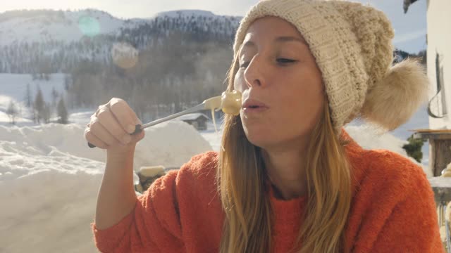 快乐的年轻女子吃芝士火锅在瑞士享受阿尔卑斯山和雪山在冬季假期。人们的饮食传统地方观念视频素材