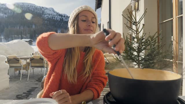 快乐的年轻女子吃芝士火锅在瑞士享受阿尔卑斯山和雪山在冬天视频素材