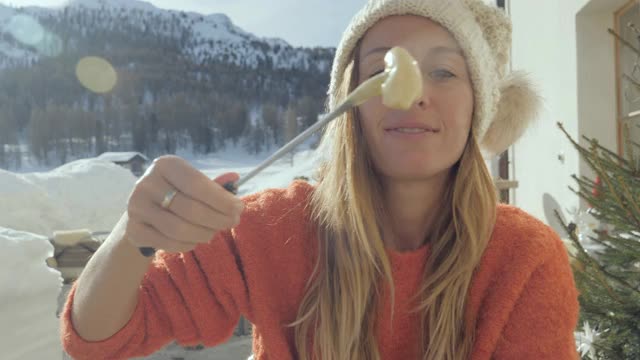 快乐的年轻女子吃芝士火锅在瑞士享受阿尔卑斯山和雪山在冬天视频素材