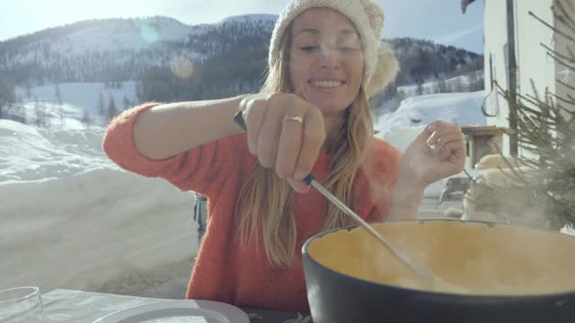 快乐的年轻女子吃芝士火锅在瑞士享受阿尔卑斯山和雪山视频素材